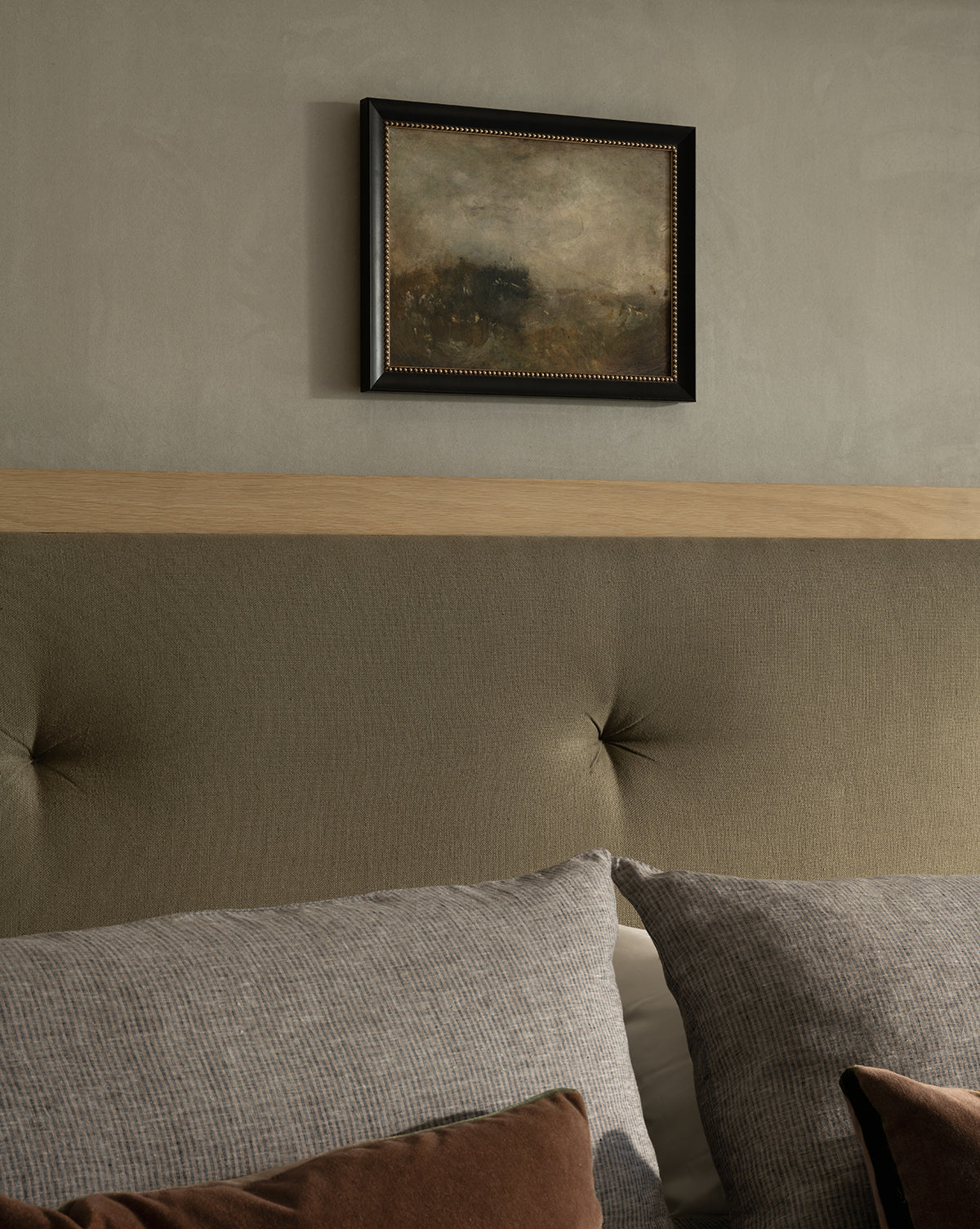The Blowing Brush framed giclee print hangs above a padded, button-tufted headboard, with gray textured pillows in front and brown accent pillows by McGee & Co. The wall is painted a soft, neutral color.