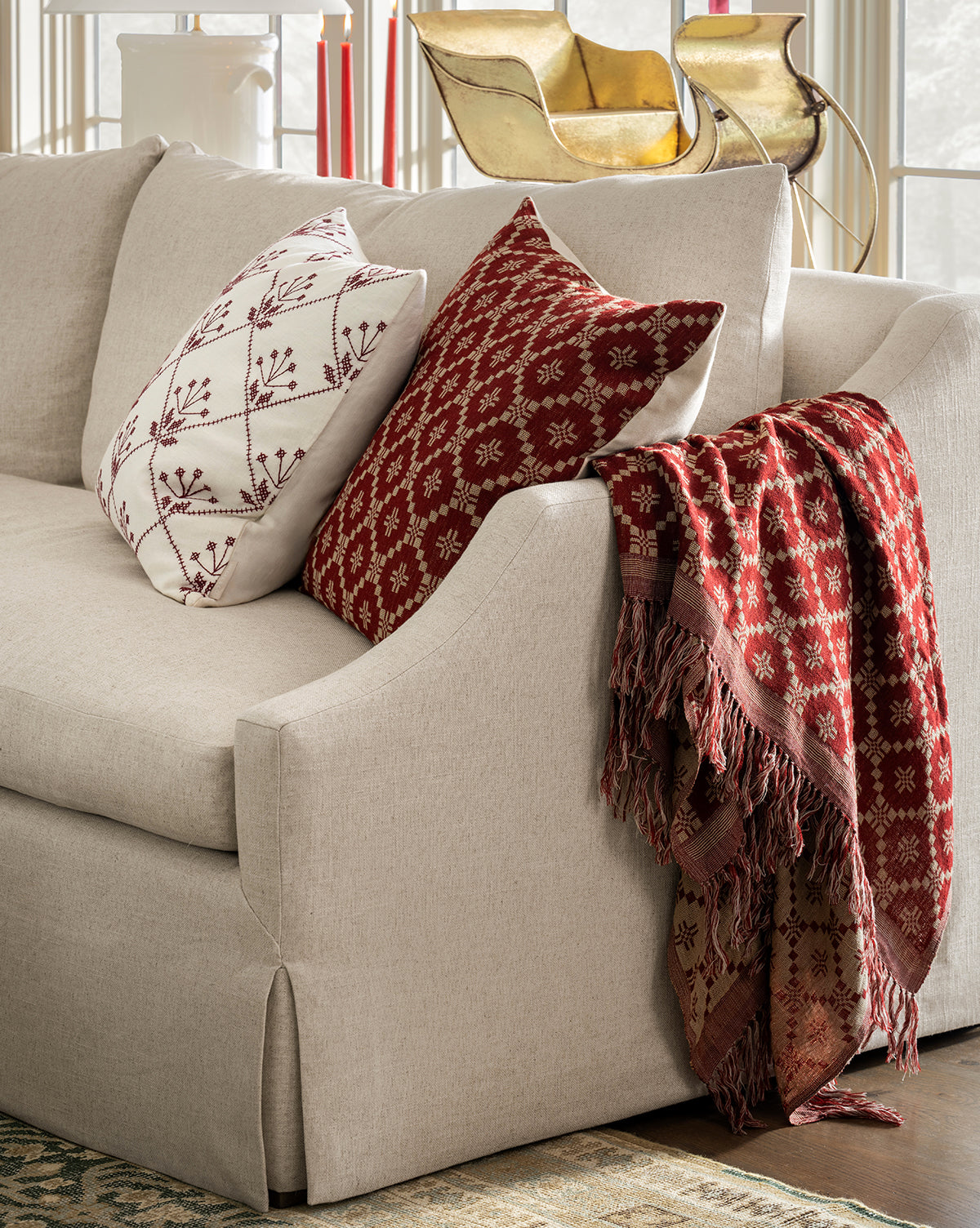 A beige sofa with two patterned throw pillows—one white with red embroidery, one red with a white geometric design—and the Jude Reversible Woven Throw draped over the armrest, by McGee & Co.