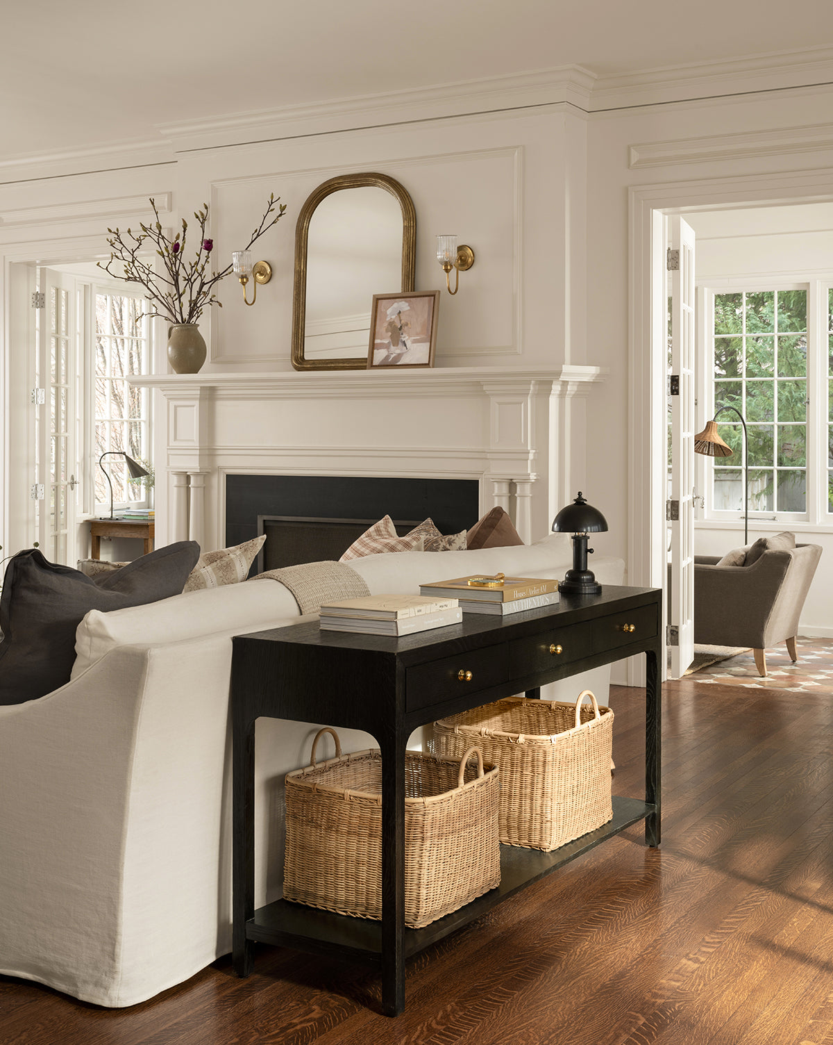 Bright living room with white walls, dark wood floors, a white sofa, black console table with baskets, fireplace topped with a mirror and decor, large windows for natural light, and a Totie Task Lamp beside the sofa by McGee & Co.