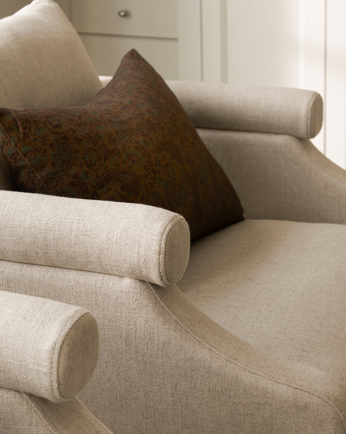 A close-up of the Clegg Lounge Chair, a beige cotton velvet armchair with rounded armrests and a dark brown patterned cushion, showcases its vintage-inspired design in soft natural light, by McGee & Co.